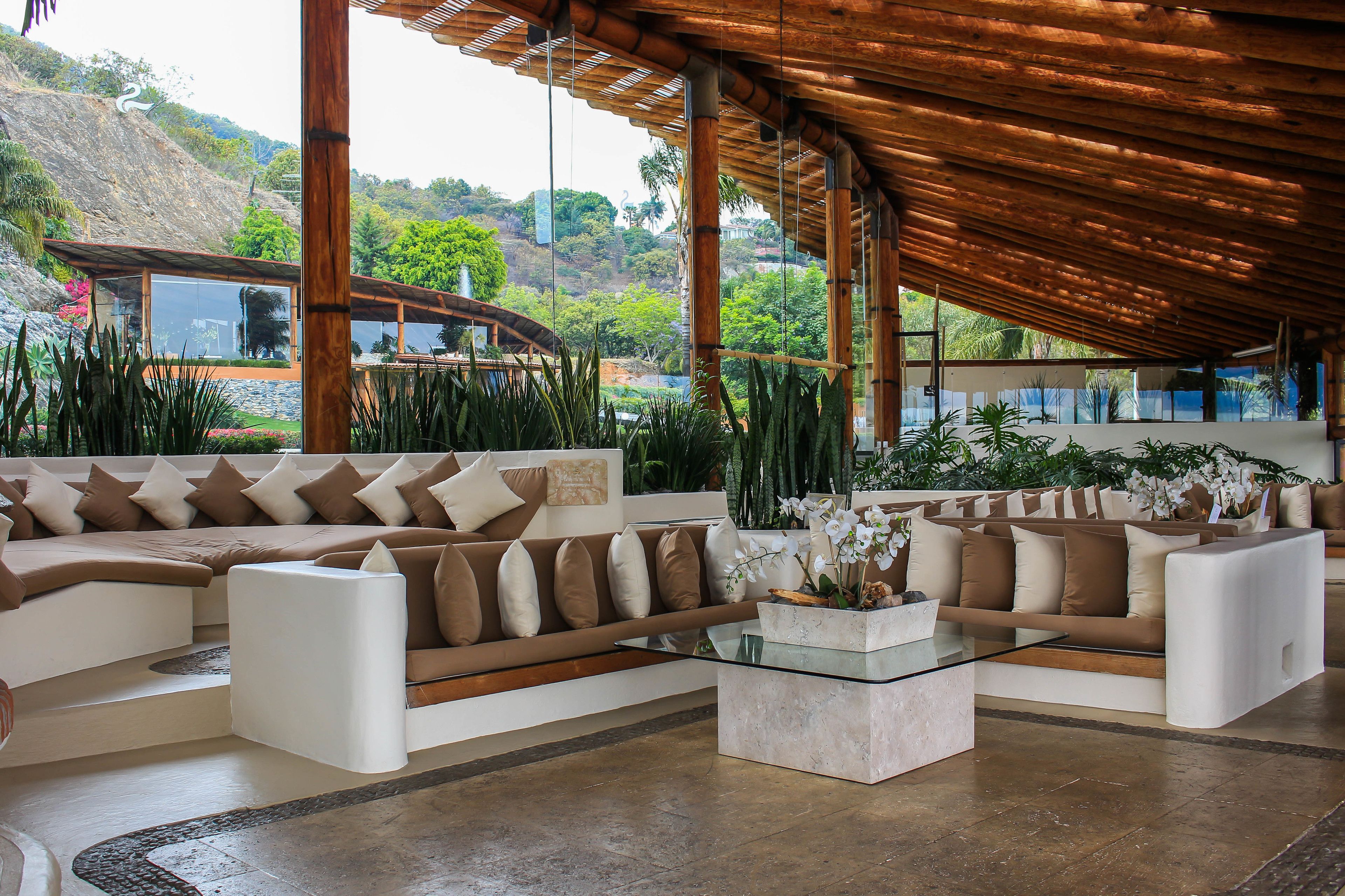 Un'area lounge moderna con un divano ampio, un tavolino in vetro e vista su un rigoglioso giardino e una collina.