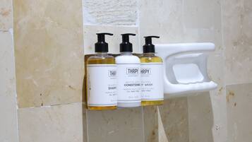 Tres botellas de Champú y Acondicionador Nutritivo Thrifty sobre un estante blanco frente a una pared de azulejos.