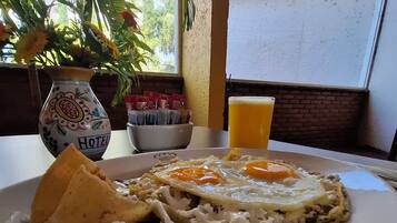 A plate of food with rice, fried eggs, and a tortilla, a glass of orange juice, and a decorative vase with a plant.