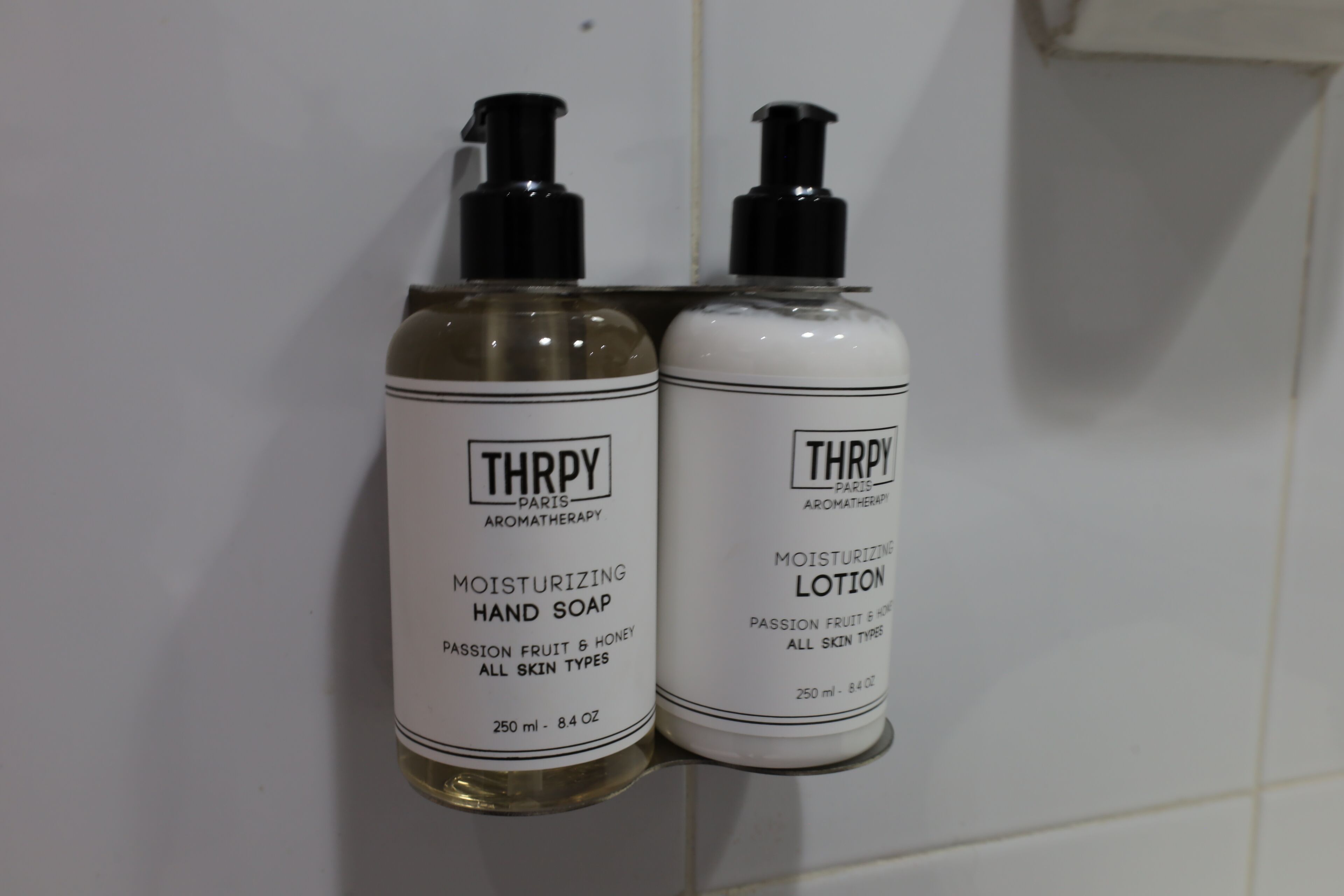 Two bottles of Thrypy aromatherapy products, one hand soap and one lotion, on a white tiled wall.