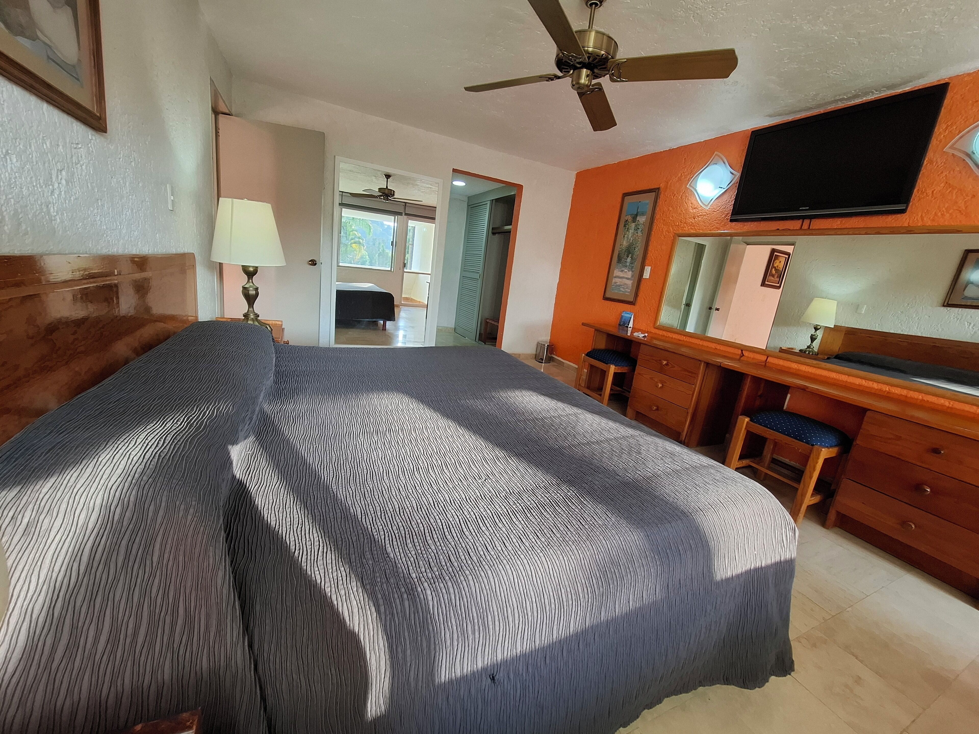 A bedroom with a bed, a desk, a chair, a television, and a ceiling fan.