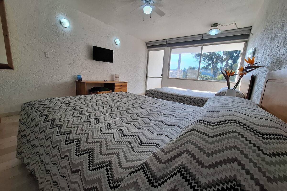 Un dormitorio con una cama grande, un escritorio, un televisor y una ventana con vistas.
