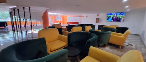 A modern lobby with yellow and green armchairs, a reception desk, and a TV screen.