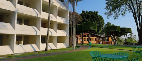 Un hotel de diseño moderno, con un patio central con sillas y mesas verdes, rodeado de césped cuidado y palmeras.
