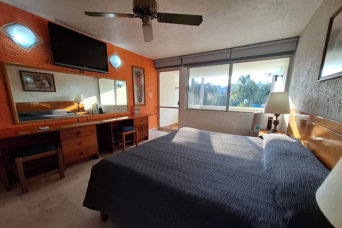 Un dormitorio con cama, escritorio, silla y un amplio ventanal.