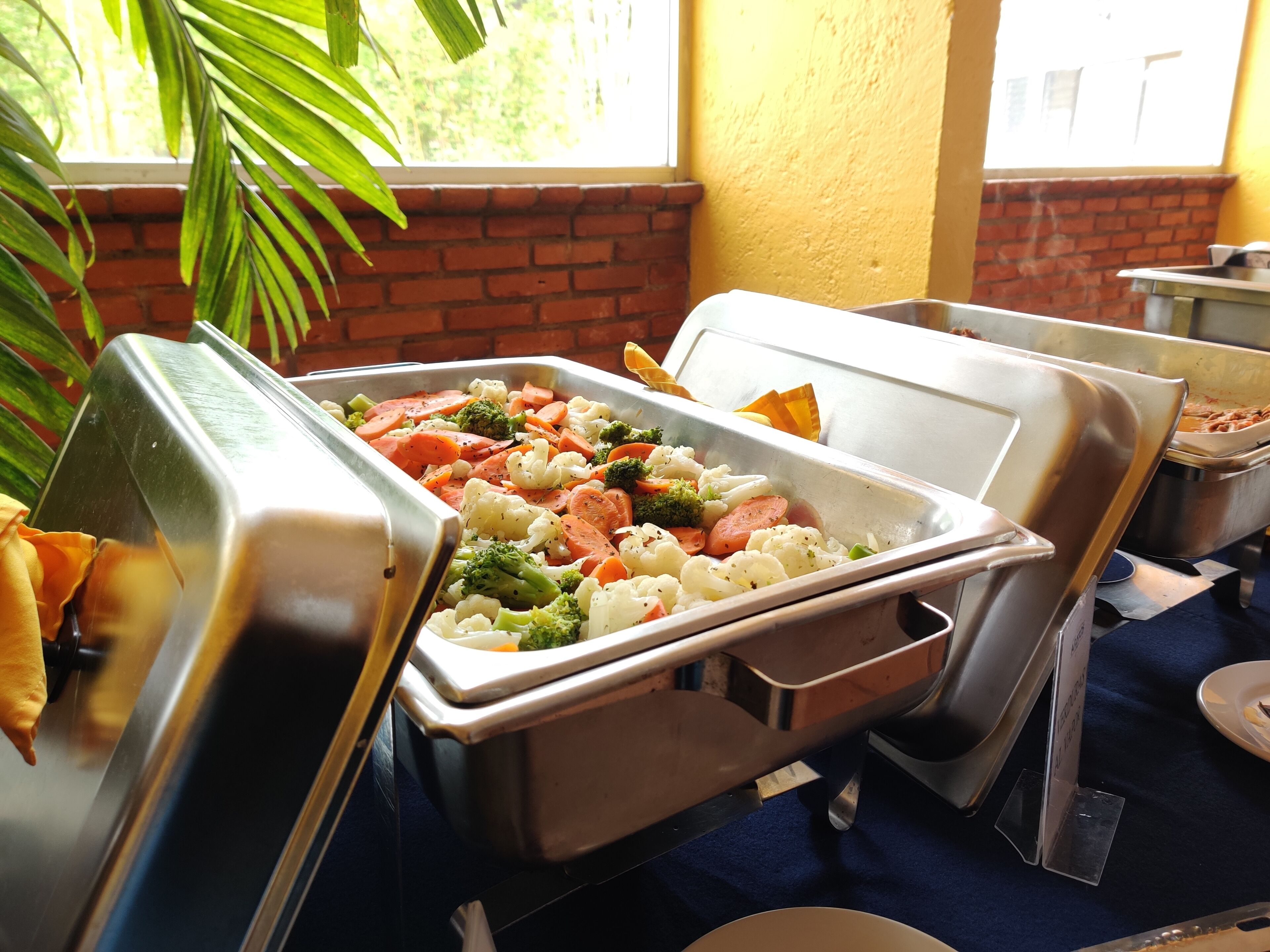 Un'impostazione buffet con diversi piatti, tra cui verdure e carni, disposti su vassoi metallici.