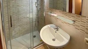 Un baño moderno con ducha envuelta en vidrio, un lavamanos blanco y un espejo encima.