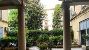 Un patio con columnas, una maceta central y un edificio al fondo.