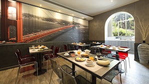 A restaurant with a large mural of the Golden Gate Bridge, multiple dining tables, and chairs. - Hotel San Francisco (Milan)