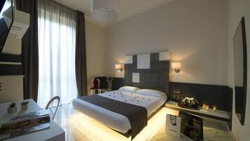 Een moderne hotelkamer met een net opgemaakt bed, een nachtkastje met een lamp, een bureau met een stoel, en een grote spiegel aan de muur.