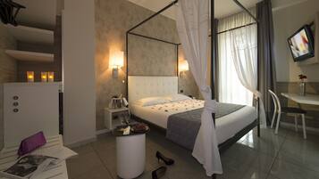 A modern hotel room with a large bed, a bedside table with a lamp, a minibar, and a TV on the wall.