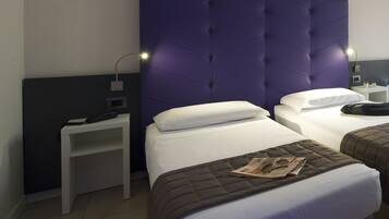 Une chambre d’hôtel avec deux lits, une table de chevet et une tête de lit moderne de couleur violette.