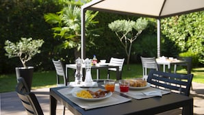 An outdoor dining area with a table set for breakfast, including plates of food, drinks, and a coffee pot. - Hotel San Francisco (Milan)