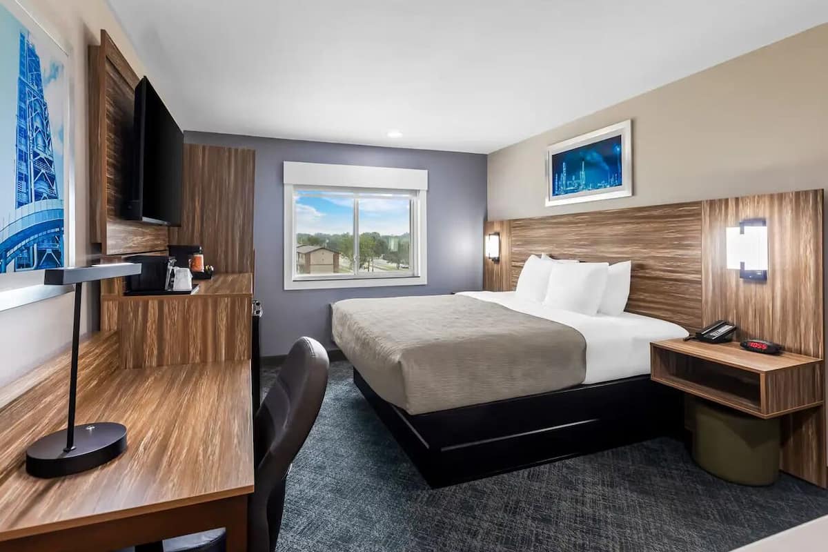 A hotel room with a bed, desk, chair, and a TV mounted on the wall.