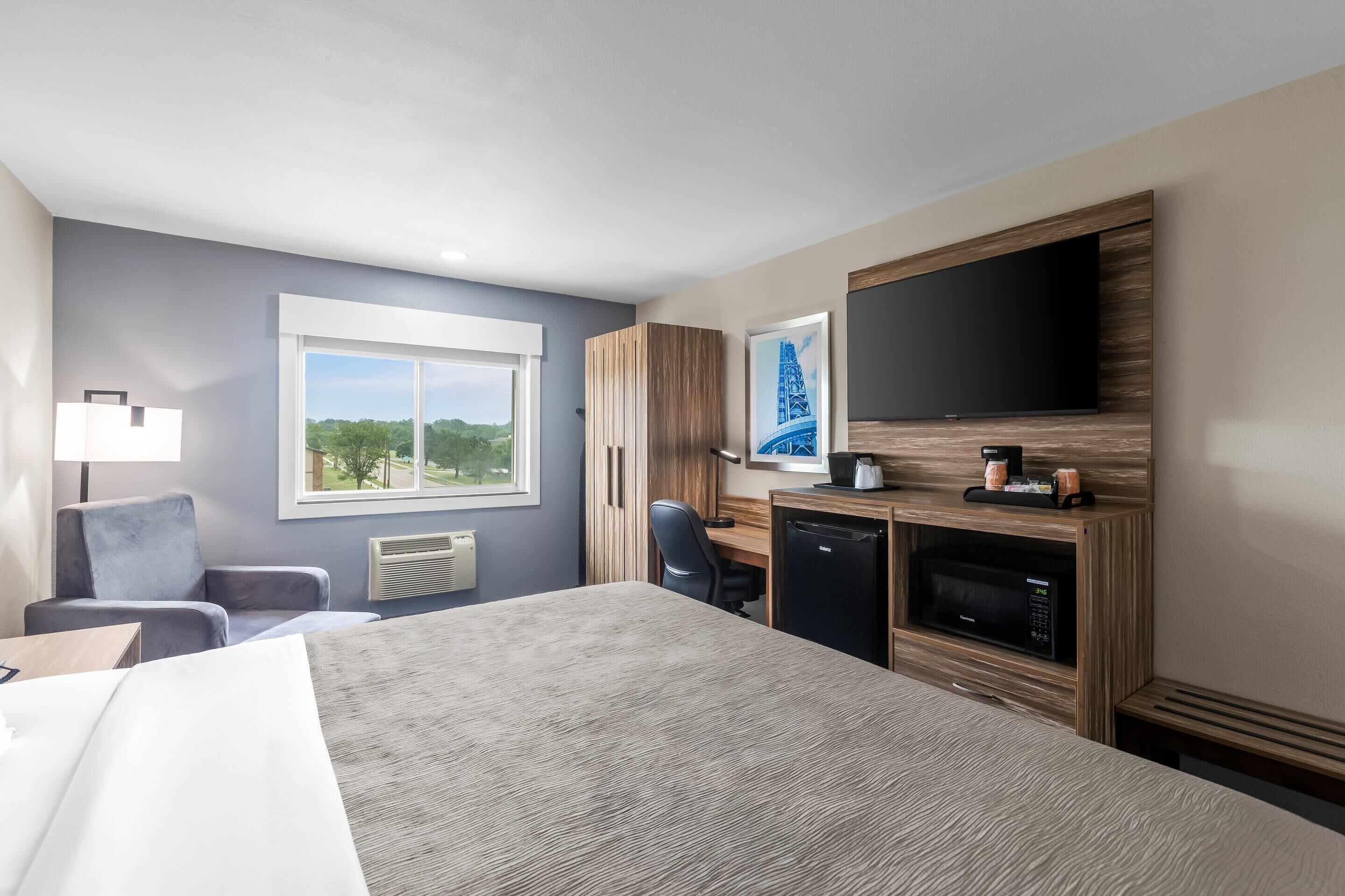 A hotel room with a bed, a desk, a chair, a TV, a microwave, and a window with a view.