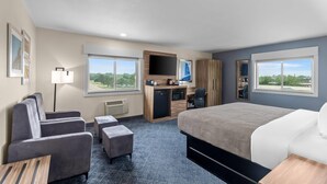 A hotel room with a bed, a desk, a chair, a sofa, and a TV.