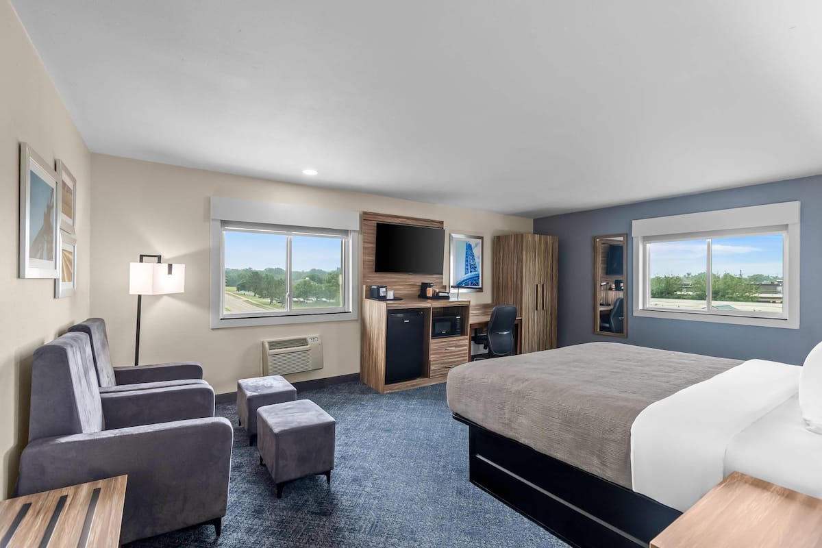 A hotel room with a bed, a desk, a chair, a sofa, and a TV.