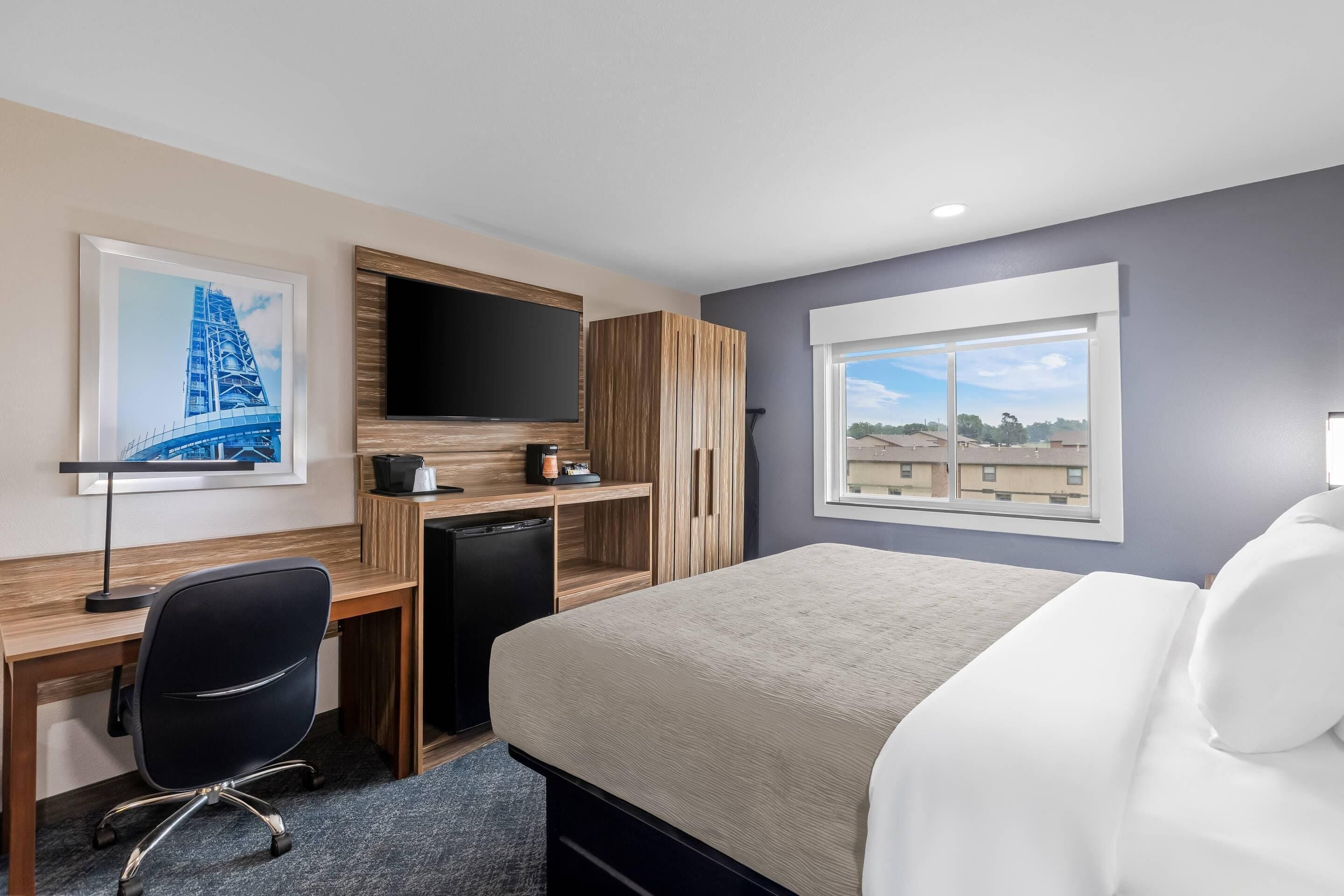 A hotel room with a bed, desk, chair, TV, and a window with a view.