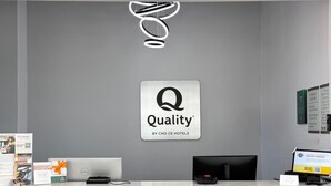 A hotel reception desk with a 'Quality' sign, a computer, a printer, and a QR code stand.