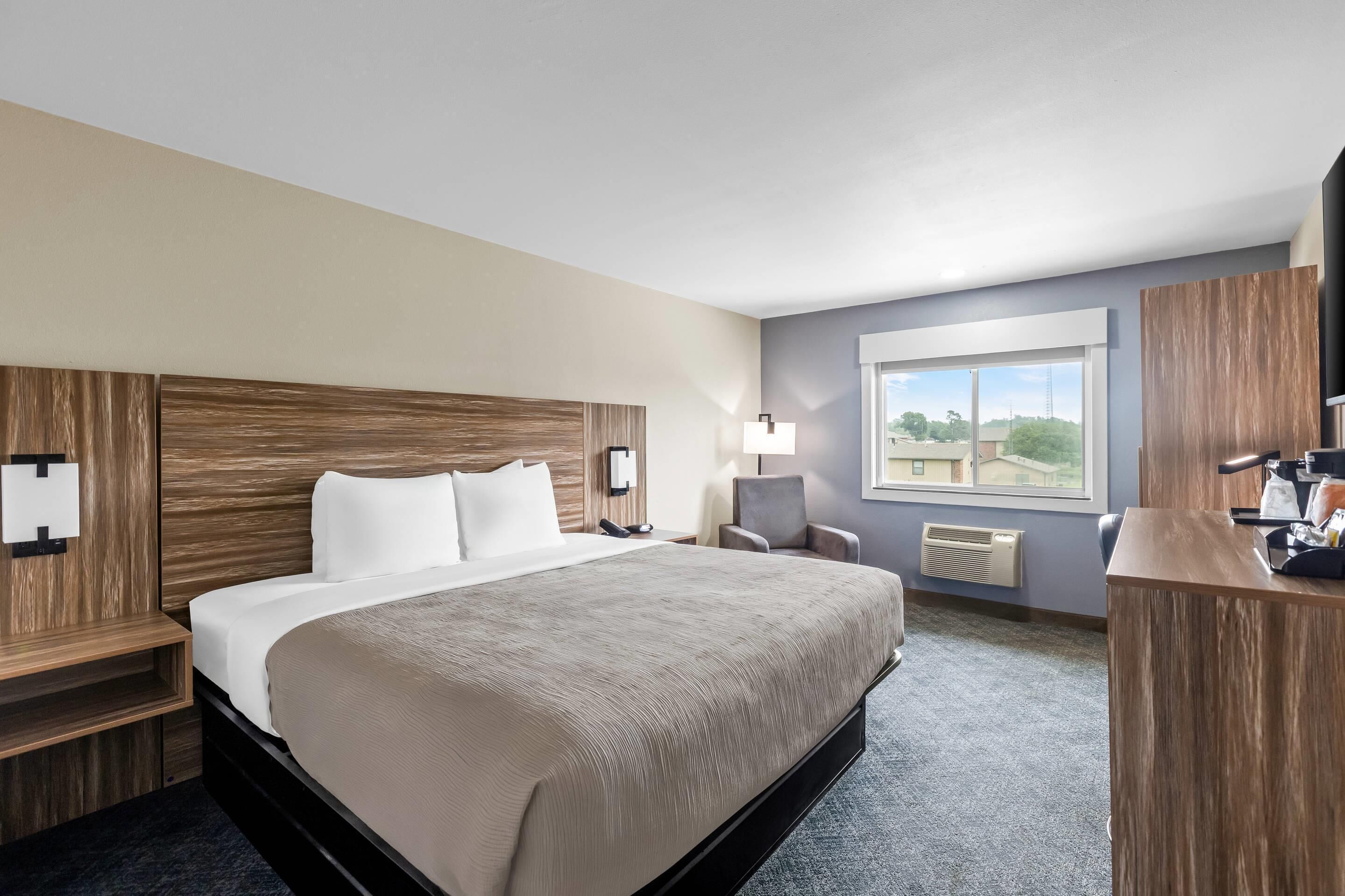 Camera d'albergo con un letto grande, una scrivania, una sedia, una televisione e una finestra con vista.