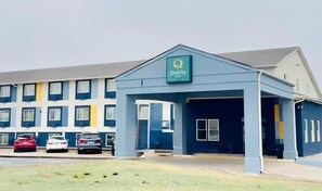A Quality Inn with a blue facade, a covered entrance, and a parking lot with three cars.