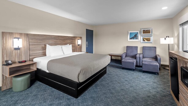 A hotel room with a bed, bedside table, lamp, chairs, and a desk.