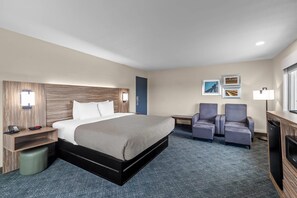 A hotel room with a bed, bedside table, lamp, chairs, and a desk.
