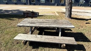 A picnic table in a grassy area with a building in the background.