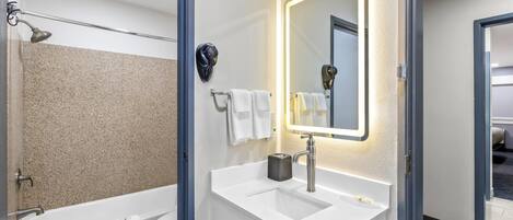 A modern bathroom with a bathtub, toilet, and sink, featuring a mirror, towel rack, and a lighted wall.