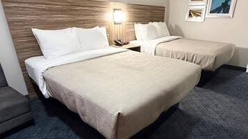A hotel room with two beds, a nightstand, a lamp, and a chair.