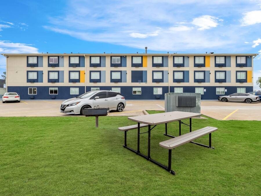 Un edificio de varios pisos con estacionamiento, una mesa de picnic y un automóvil estacionado al frente.