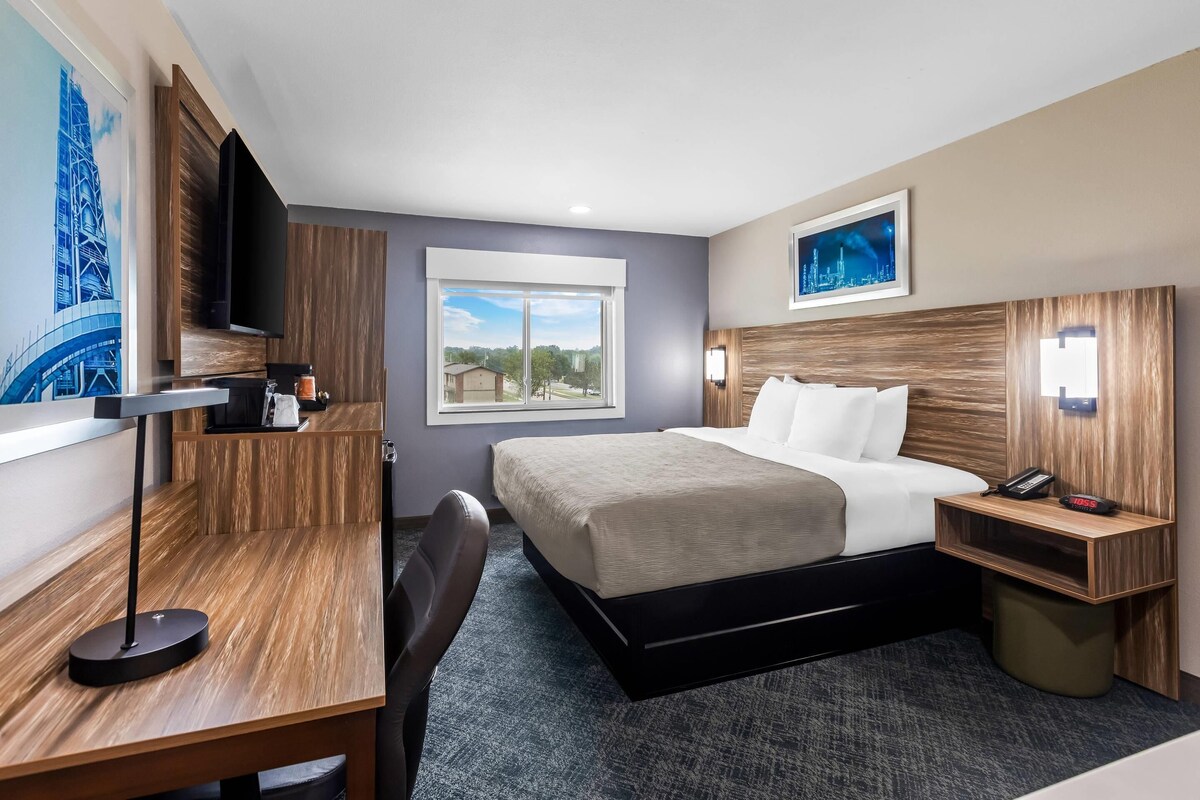 A hotel room with a bed, desk, chair, and a window with a view.