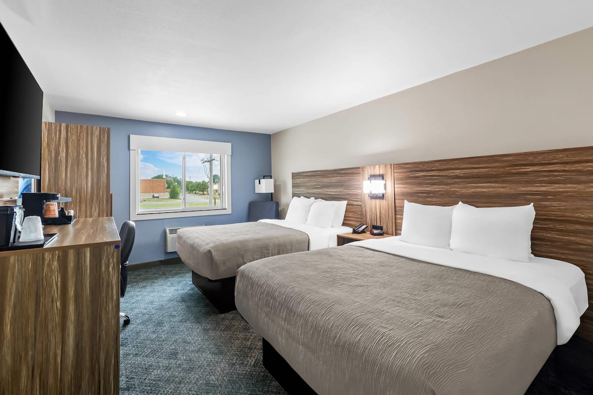 A hotel room with two beds, a desk, a chair, a window with a view, and a wooden headboard.