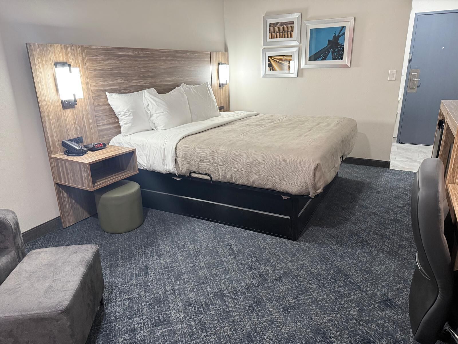 A hotel room with a bed, bedside table, lamp, and a desk with a chair.