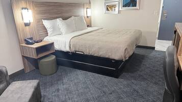 A hotel room with a bed, bedside table, lamp, and a desk with a chair.