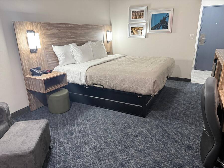 A hotel room with a bed, bedside table, lamp, and a desk with a chair.