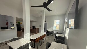 A modern dining area with marble tables and black chairs, a kitchen in the background, and a ceiling fan.