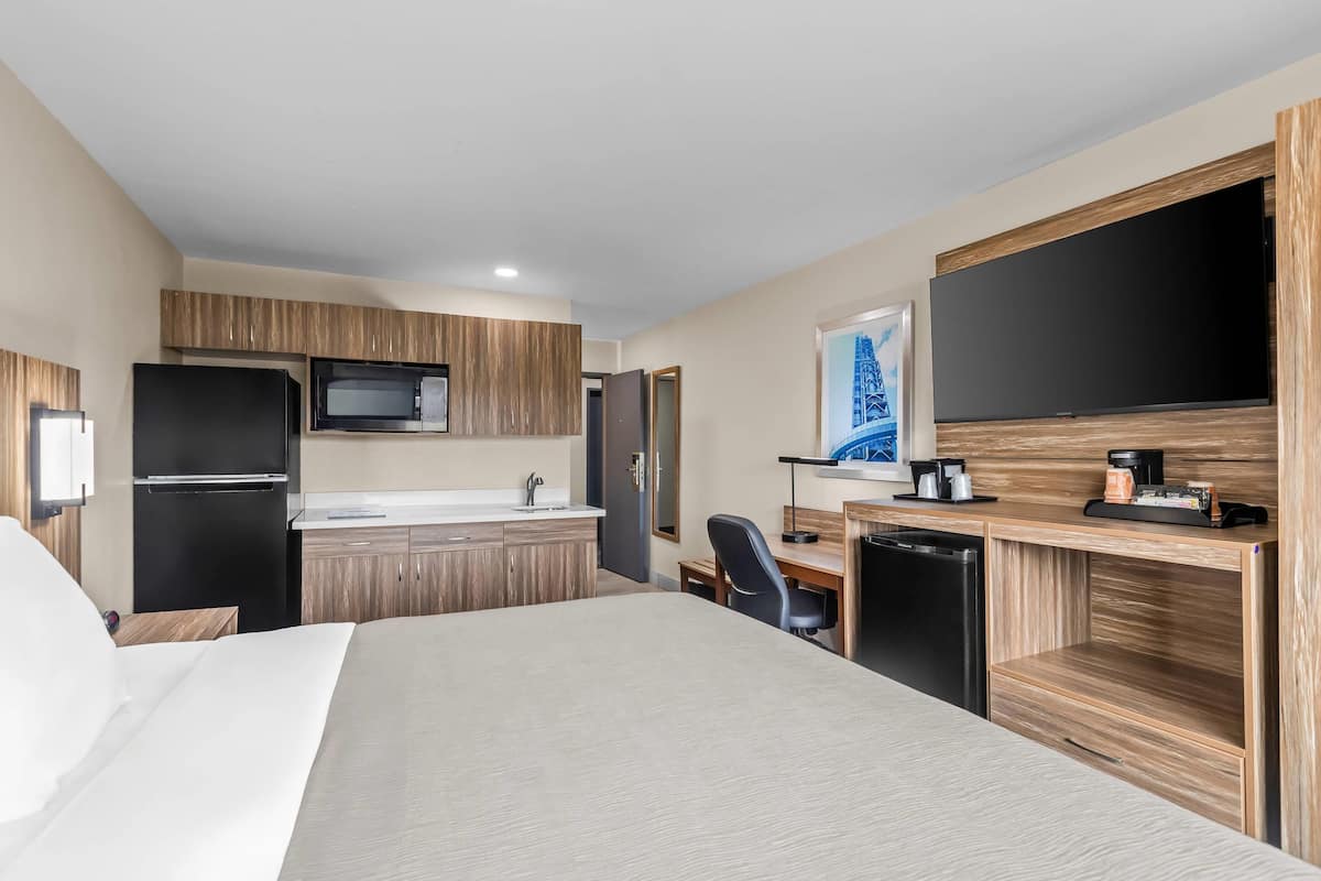 A hotel room with a bed, kitchenette, desk, and a large TV.