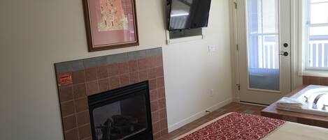 A hotel room with a fireplace, a mounted TV, a door with a view, and a patterned rug.