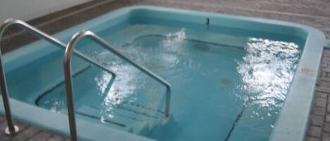 A small indoor pool with a metal ladder and a white table in the background.