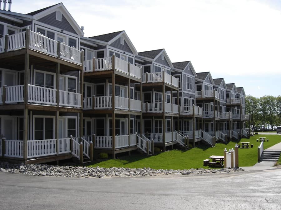 A row of multi-story buildings with balconies, a grassy area in front, and a paved road.