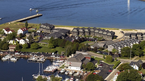 Un puerto deportivo con barcos, un faro y una zona residencial con casas y un estacionamiento.
