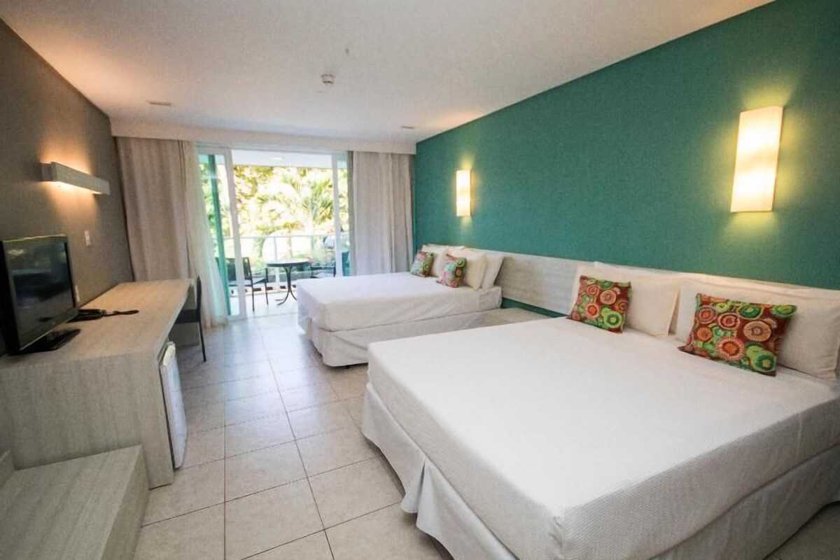 A hotel room with two beds, a desk, a television, and a view of the outdoors.