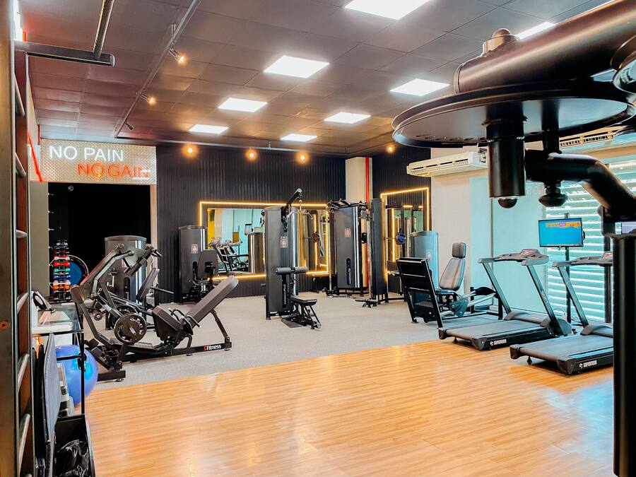 Un gimnasio con varios equipos de ejercicio, una cinta de correr y un cartel que dice 'NO PAIN NO GAIN'.