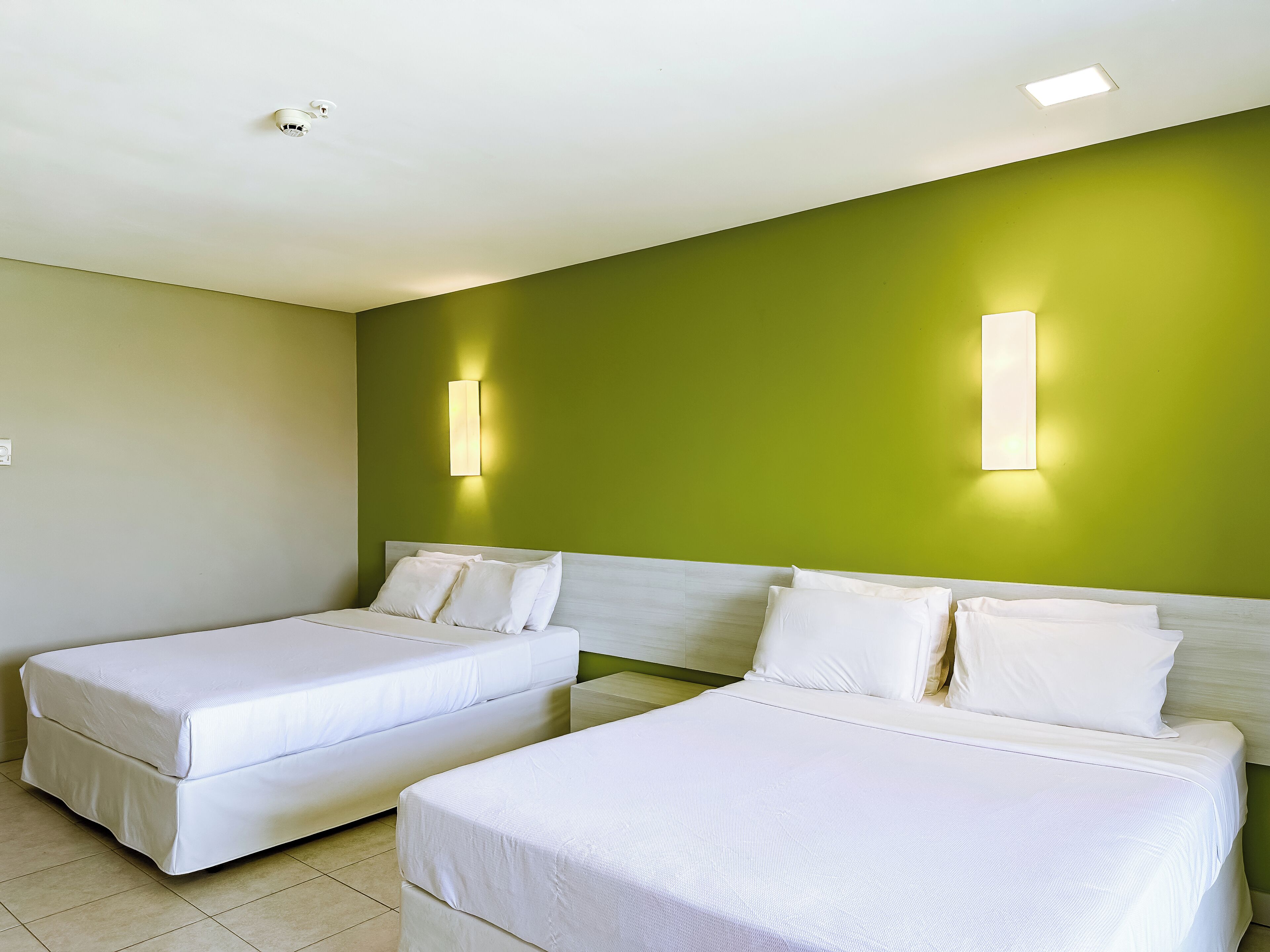 A hotel room with two single beds, a green accent wall, and two wall-mounted light fixtures.