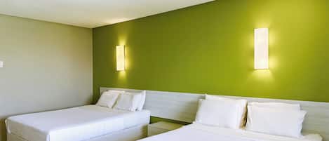 A hotel room with two single beds, a green accent wall, and two wall-mounted light fixtures.