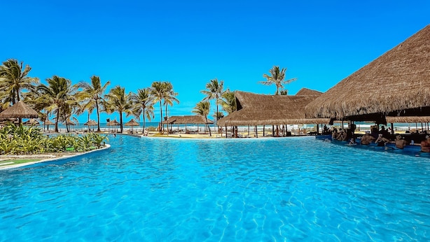 Una piscina azul cristalina con estructuras de techo de paja y palmeras.