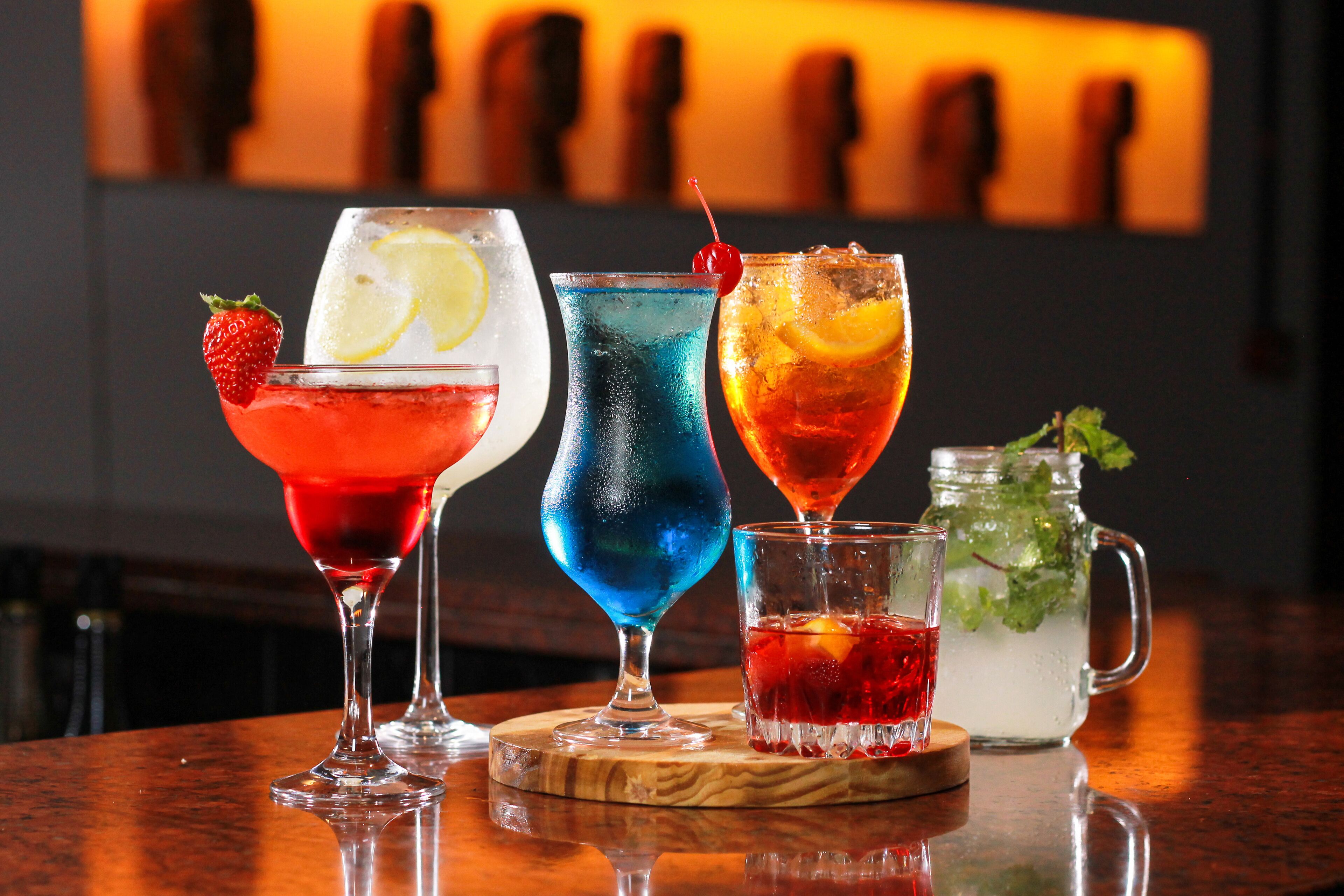 Vier Cocktails auf einer Holztresen, unscharfer Hintergrund.