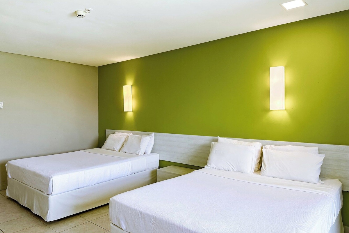 A hotel room with two beds, a green accent wall, and two wall-mounted light fixtures.