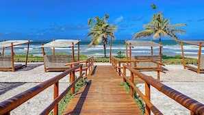 Un paseo marítimo de madera que conduce a sombrillas y sillas de playa, con palmeras y vistas al océano.